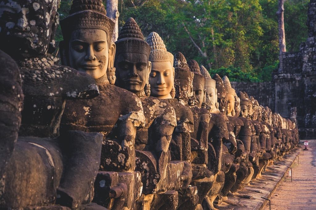 Stone statues of gods and demons at the entrance of Angkor Thom, Cambodia, bathed in warm sunlight.