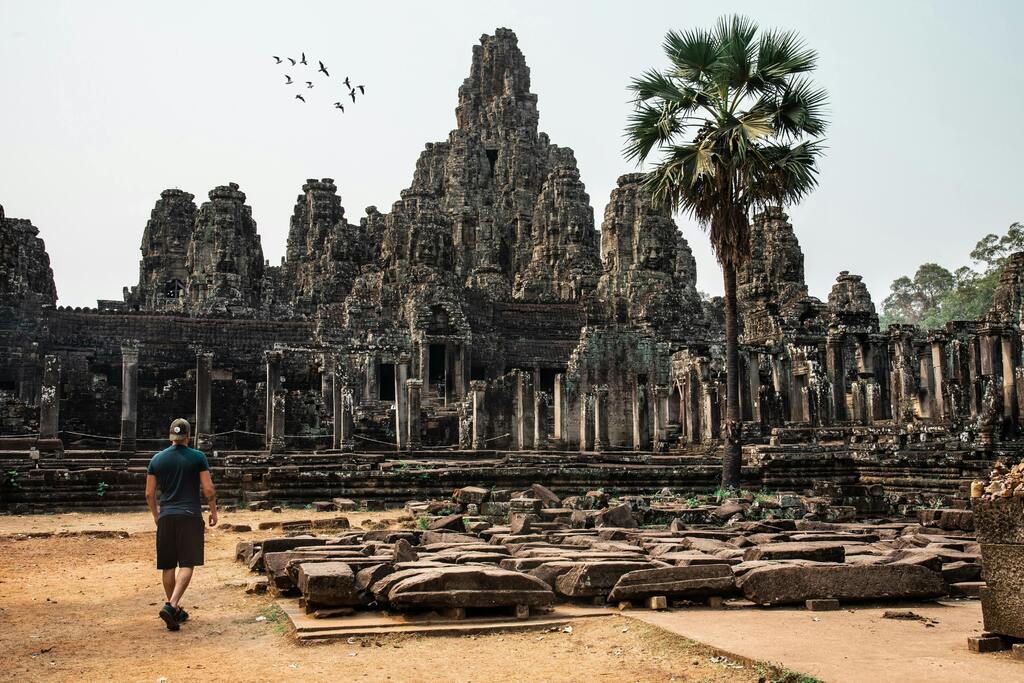 Ancient ruins of Bayon Temple in Angkor Thom, Cambodia, with a lone traveler exploring the site.