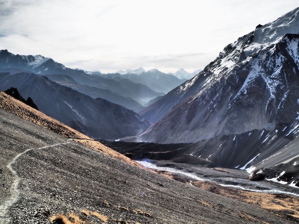 A rugged mountain path in the Annapurna region, Nepal, with snow-capped peaks and deep valleys stretching into the distance.