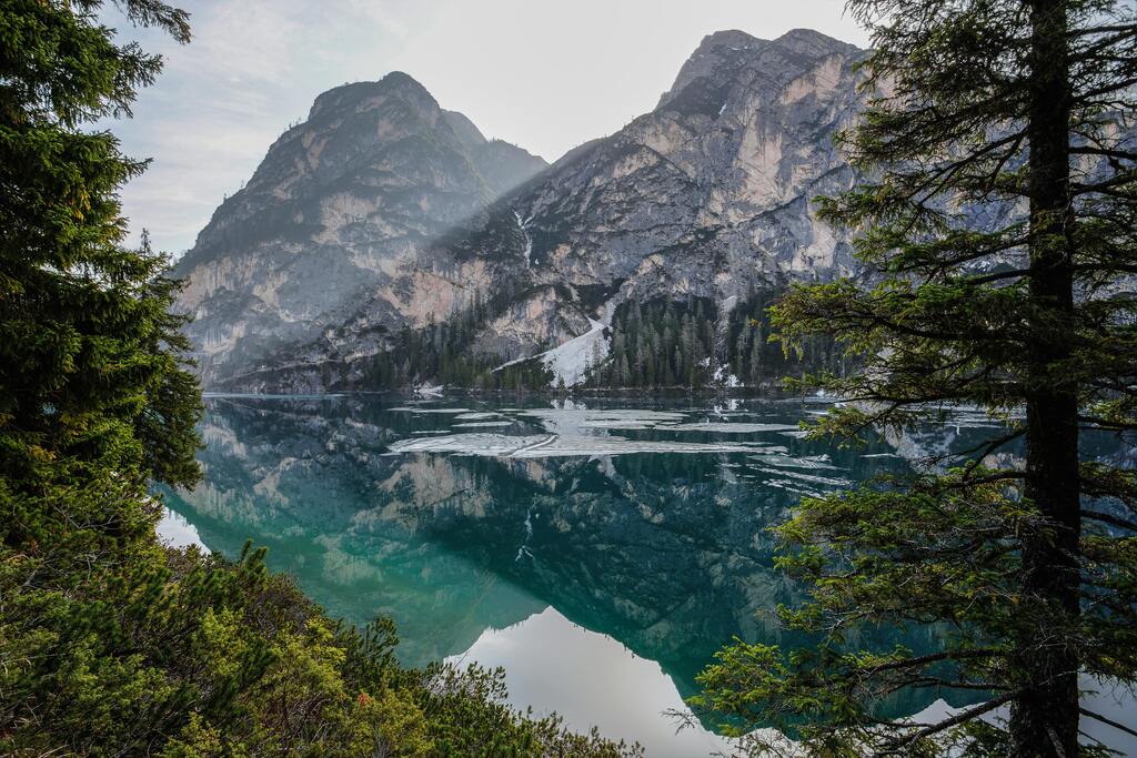 A serene lake in the Dolomites, Italy, reflecting towering mountains and evergreen trees in its crystal-clear waters.