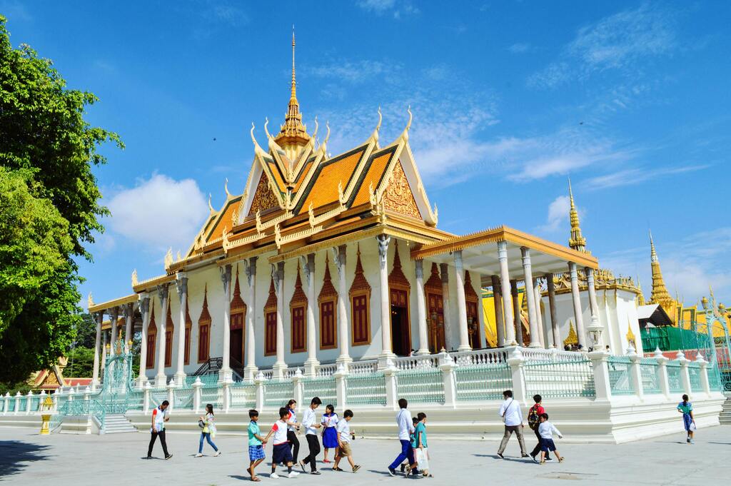 The Silver Pagoda in Phnom Penh, Cambodia, with tourists and schoolchildren walking in front of the ornate golden temple.
