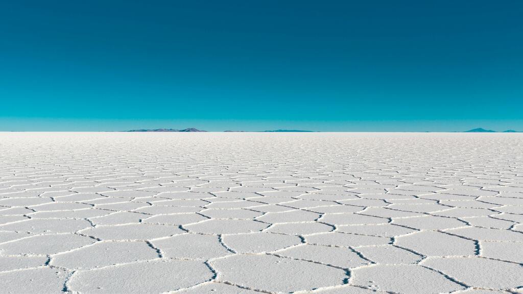 The endless white salt flats of Salar de Uyuni in Bolivia, with a hexagonal pattern of salt formations stretching toward the horizon under a deep blue sky.