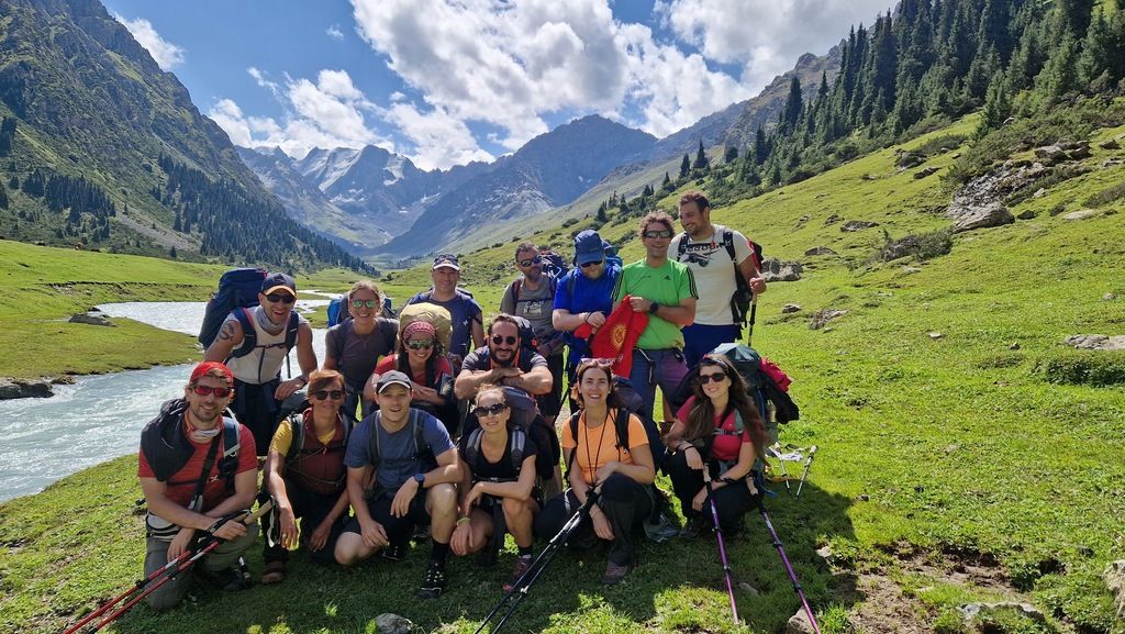  A group of hikers posing in front of a river with the stunning backdrop of the Tian Shan mountains in Kyrgyzstan.