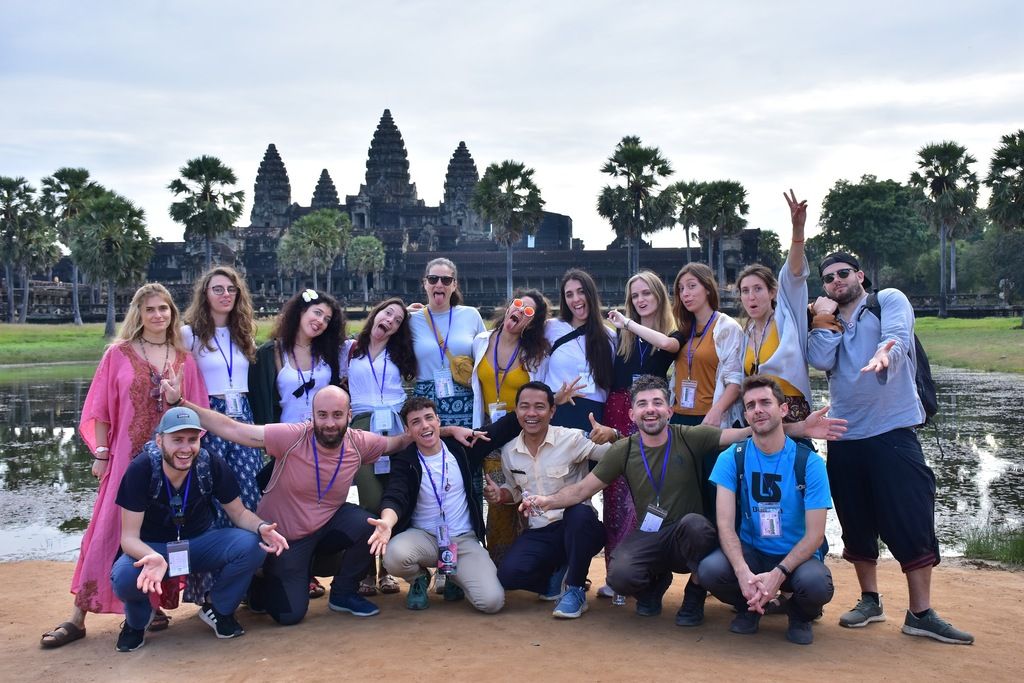 A lively WeRoad group tour in Cambodia posing in front of Angkor Wat, excited and enjoying their adventure.