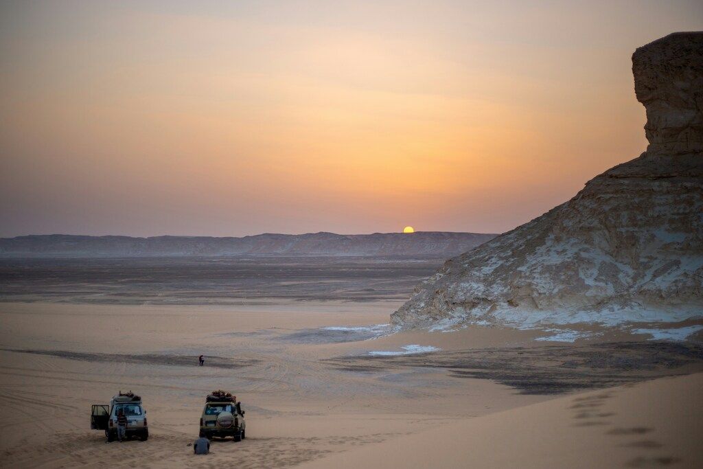 Sunset over the Egyptian desert with two off-road vehicles and sandstone cliffs.