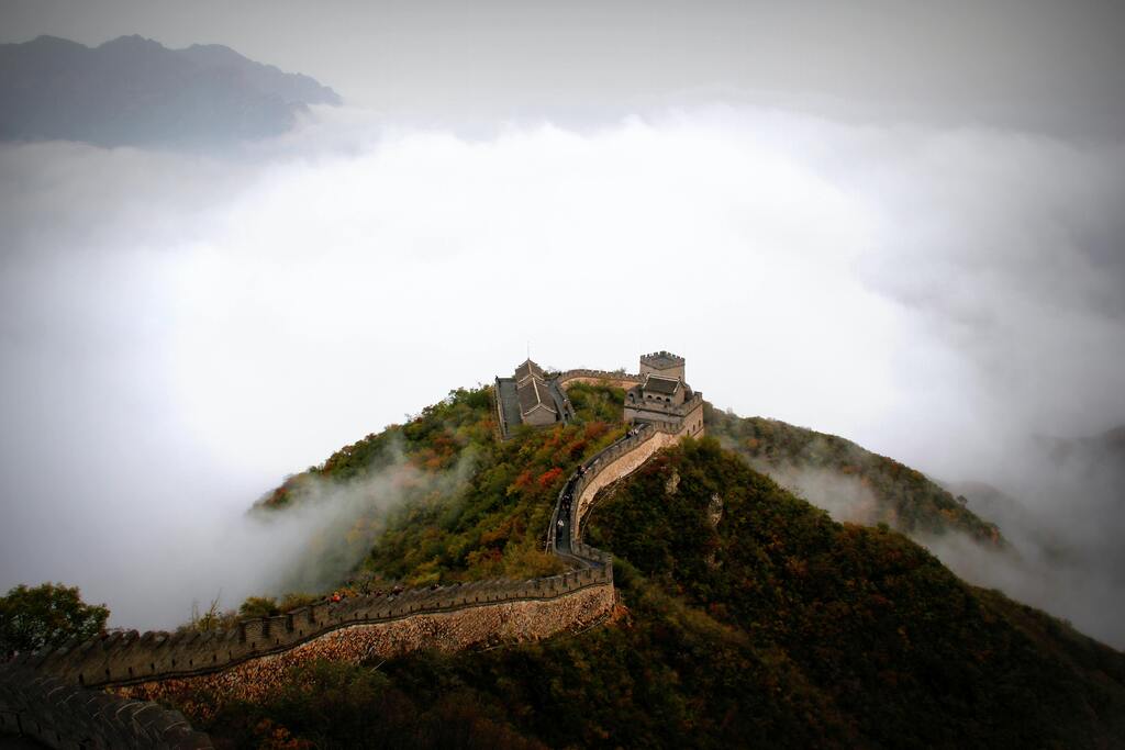 Aerial view of the Great Wall of China surrounded by clouds and autumn colors.