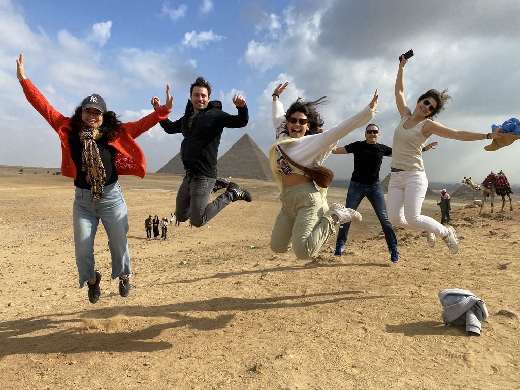 Group of WeRoad travelers during a group tour in Egipt, jumping in front of the pyramids of Giza.