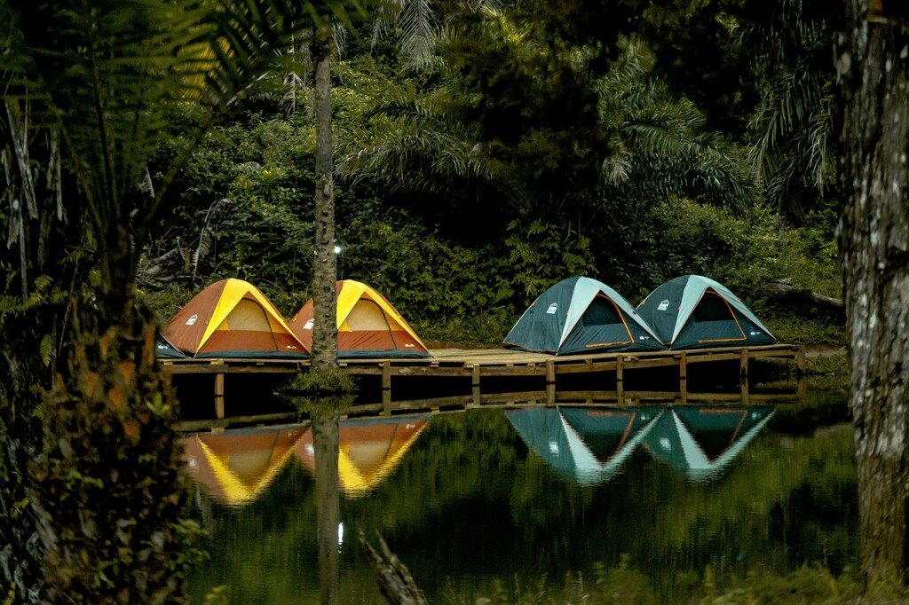 Four colorful tents reflected in a calm jungle river surrounded by lush vegetation