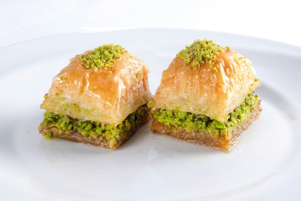 Two pieces of baklava topped with crushed pistachios on a white plate.