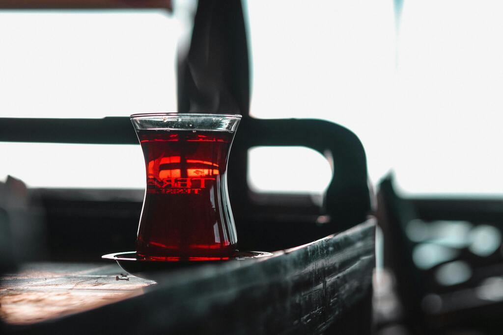 A glass of Turkish tea (Çay) on a dark wooden surface with a blurred background. mbol