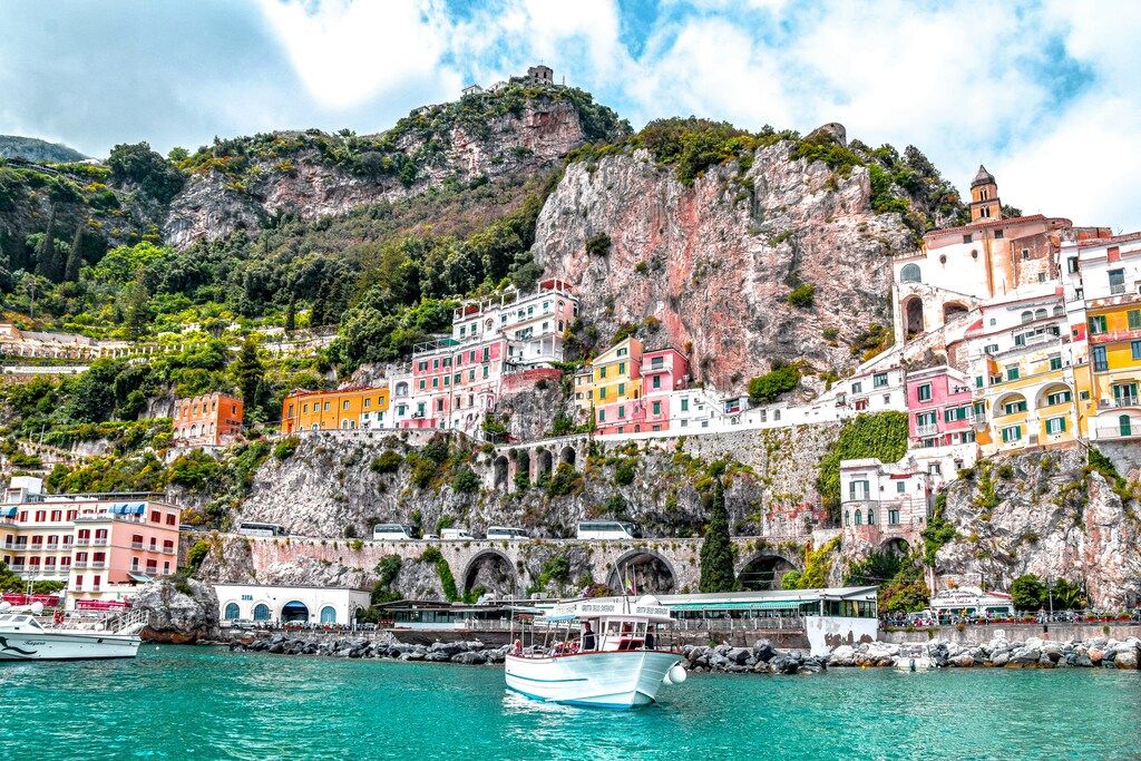 Colorful cliffside buildings overlooking the turquoise sea along the Amalfi Coast, with boats docked at the shore.