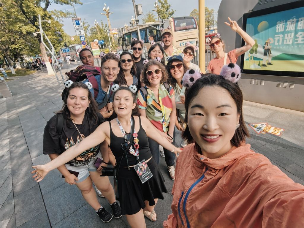 Happy group of WeRoad travelers posing for a selfie during a city tour in China, wearing panda-themed accessories.