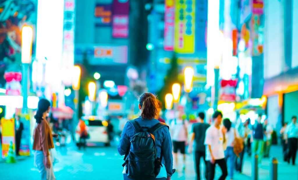 Traveler with a backpack walking through a vibrant, neon-lit street in Tokyo at night.