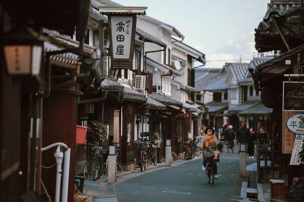 Peaceful traditional Japanese street with wooden houses, where a woman rides a bicycle and locals walk by.