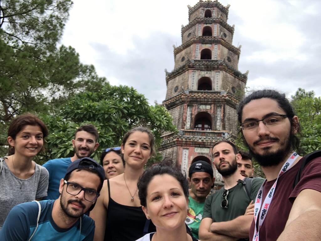 WeRoad travelers taking a group selfie in front of the iconic Thien Mu Pagoda in Hue, Vietnam.