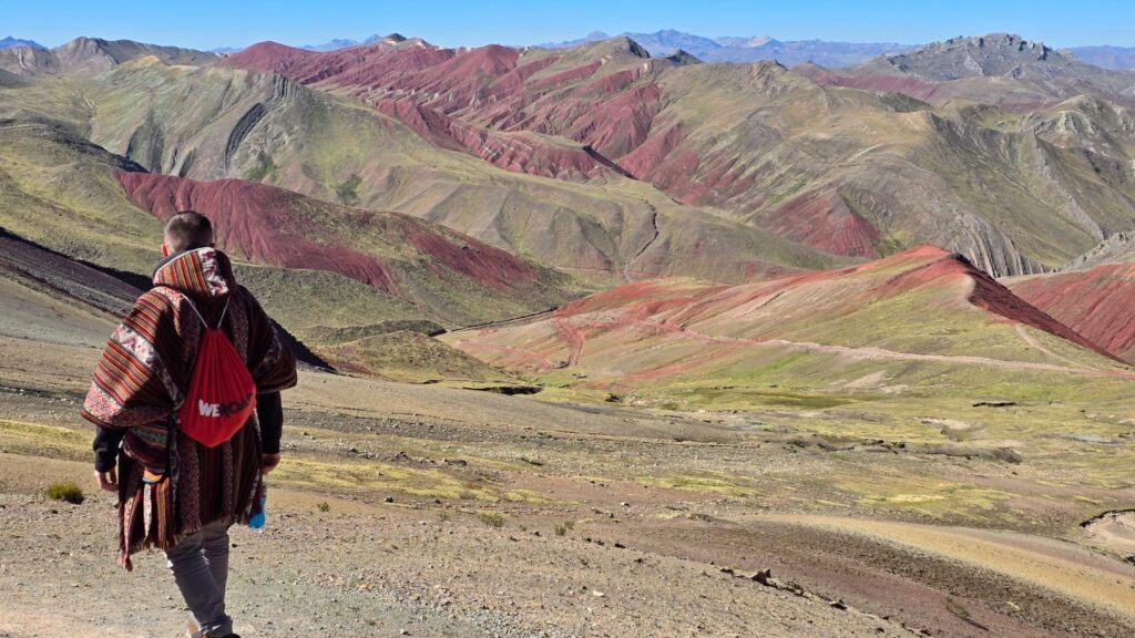WeRoad Hiker wearing traditional poncho overlooks colorful Peruvian mountain landscape.