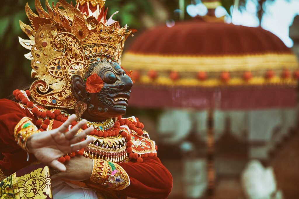 Balinese dancer in traditional gilded mask and ornate red costume.