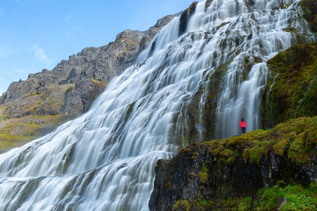 Dynjandi waterfall cascading over tiered rocks with a person in a red jacket.