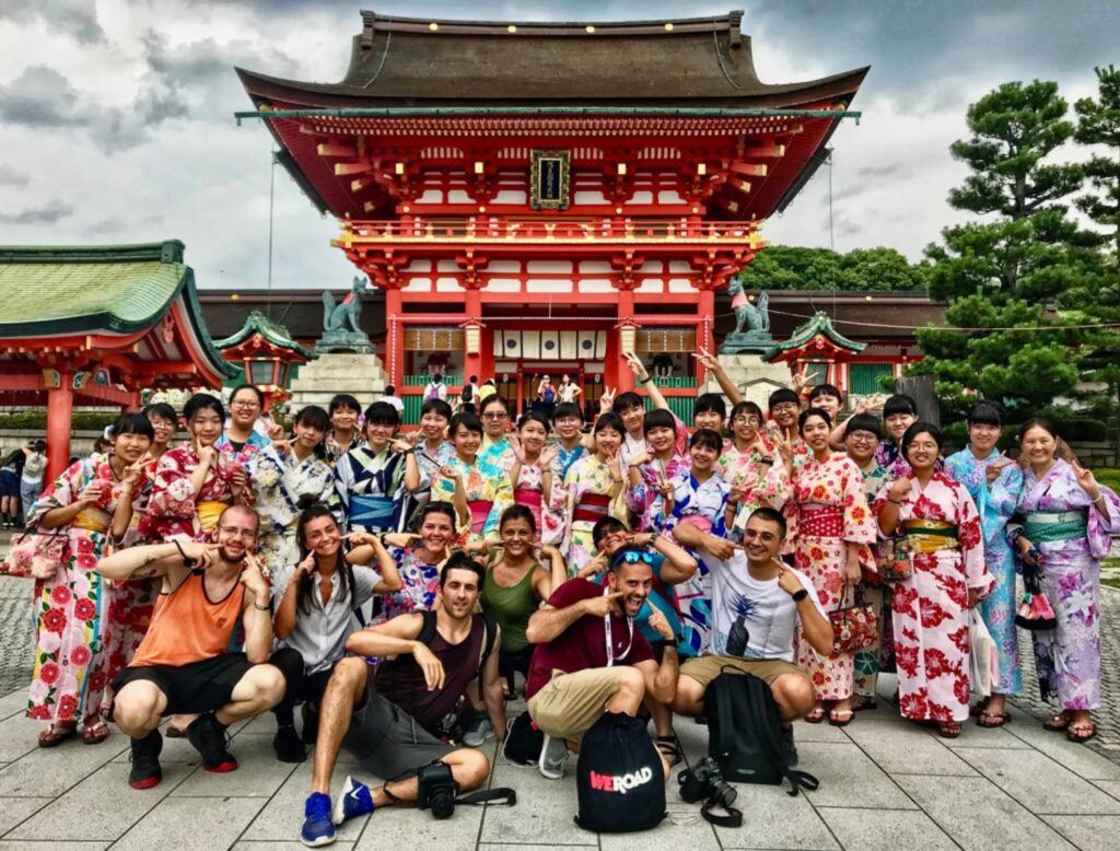 WeRoad travellers and local women in kimonos posing in front of a red Japanese temple.