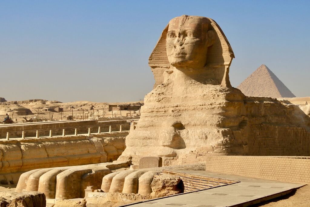 The Great Sphinx of Giza, a massive limestone statue with the body of a lion and a human head, with a pyramid visible in the background.