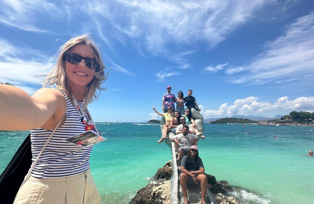 Des voyageurs WeRoad sur une main en pierre à Ksamil, une magnifique plage d'Albanie aux eaux turquoise.