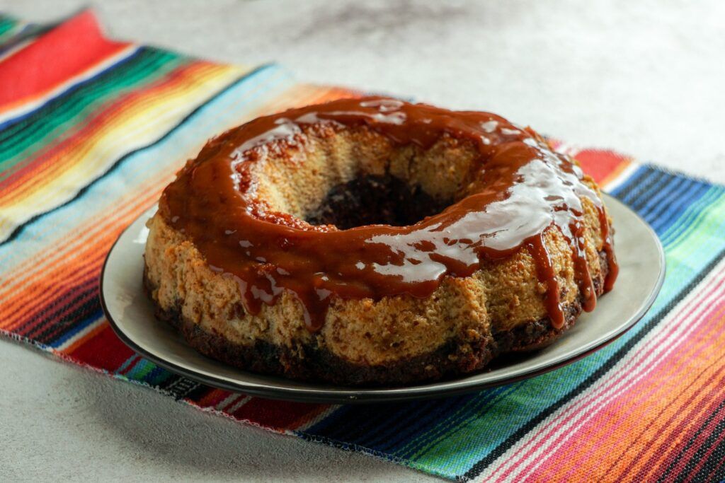A Mexican Chocoflan, also known as 'Impossible Cake', topped with caramel sauce and served on a colorful striped zarape cloth.
