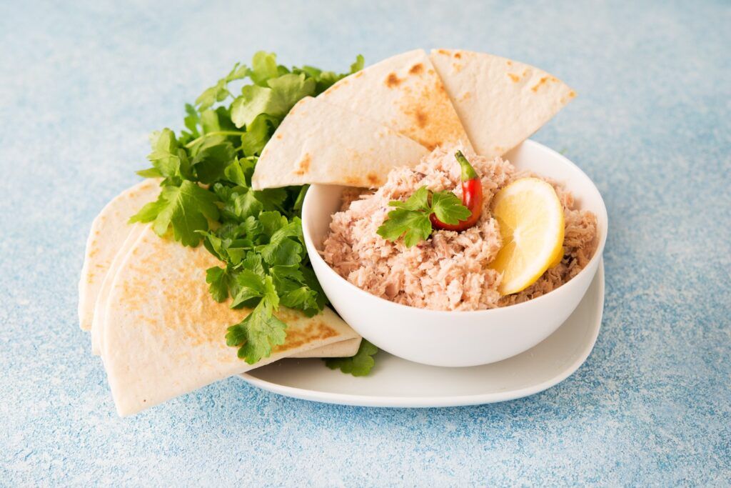 A bowl of Mas Huni: a tuna salad garnished with a lemon slice and red chili, served with pita bread triangles and fresh parsley.