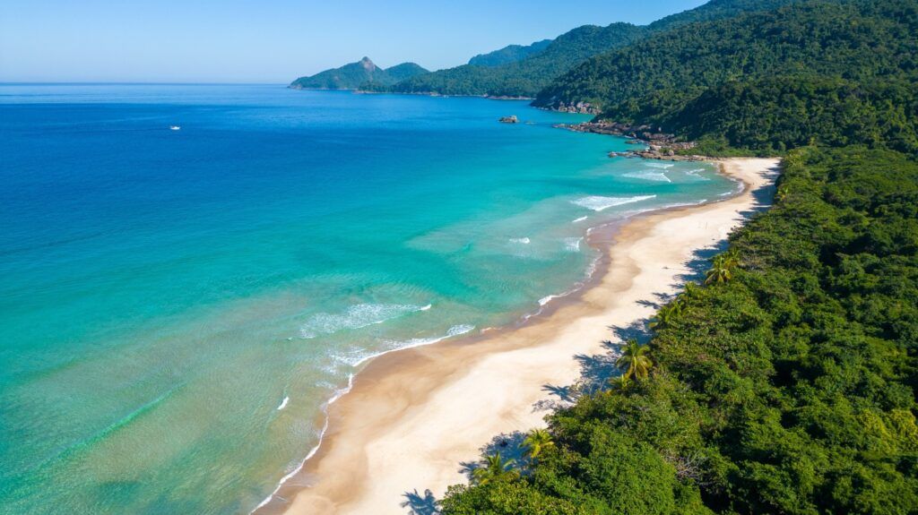 An aerial view of the pristine Lopes Mendes Beach in Brazil, featuring white sand, turquoise water, and a lush green forest backdrop.