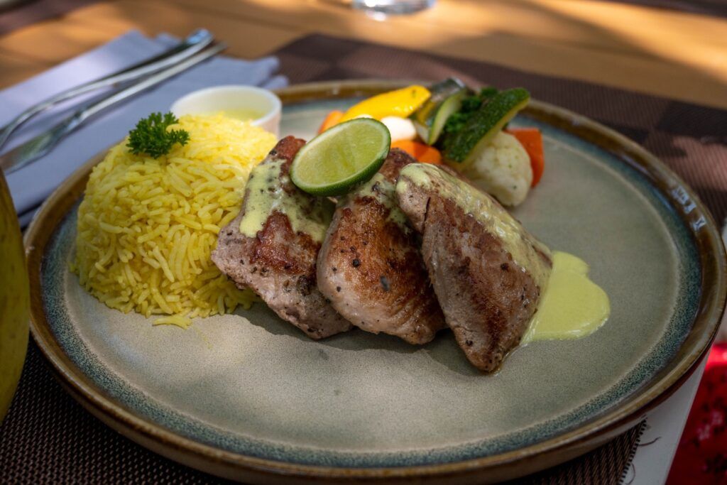 Seared tuna steaks topped with a creamy sauce and lime, served with yellow rice and sautéed vegetables.