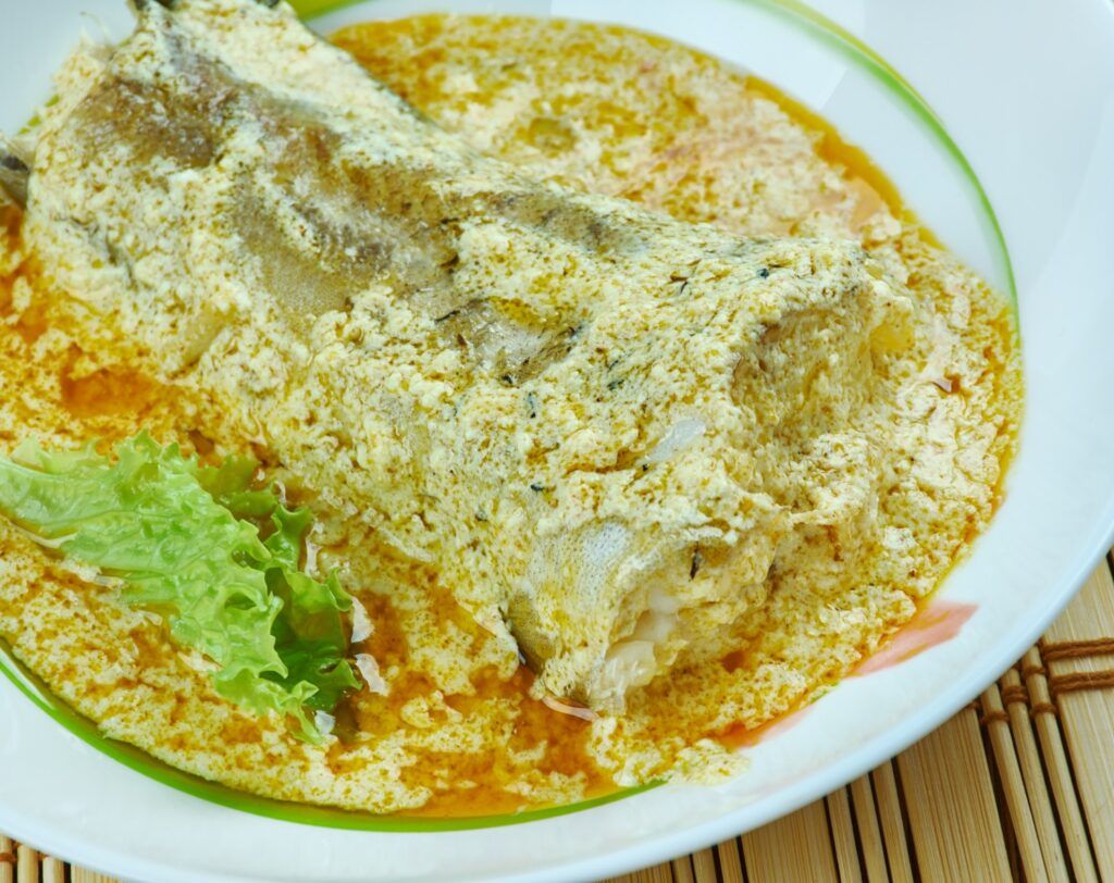 Poached fish fillet served in a rich, creamy yellow curry sauce with a side of fresh lettuce.