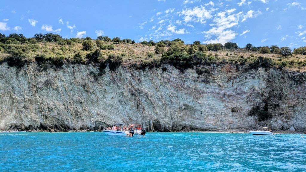 Bateaux d’excursion flottant sur une eau turquoise lumineuse à côté d’une falaise de calcaire massive, rayée unique en Albanie.